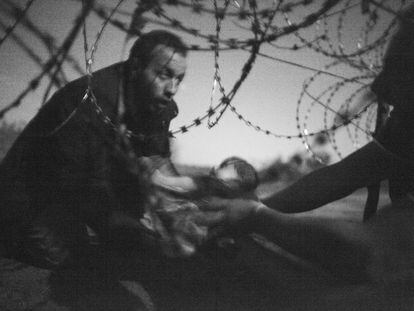 Esta imagem do fotógrafo australiano Warren Richardson foi considerada a melhor foto do ano na 59a edição do World Press Photo, a maior premiação do fotojornalismo mundial. A fotografia, em preto e branco, mostra um homem passando um bebê pela cerca de arame farpado em Roeszke, na fronteira entre a Sérvia e a Hungria, em 28 de agosto de 2015.