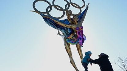Homem brinca com criança ao lado de escultura com os anéis olímpicos no Parque de Shougang, em Pequim, nesta terça-feira.