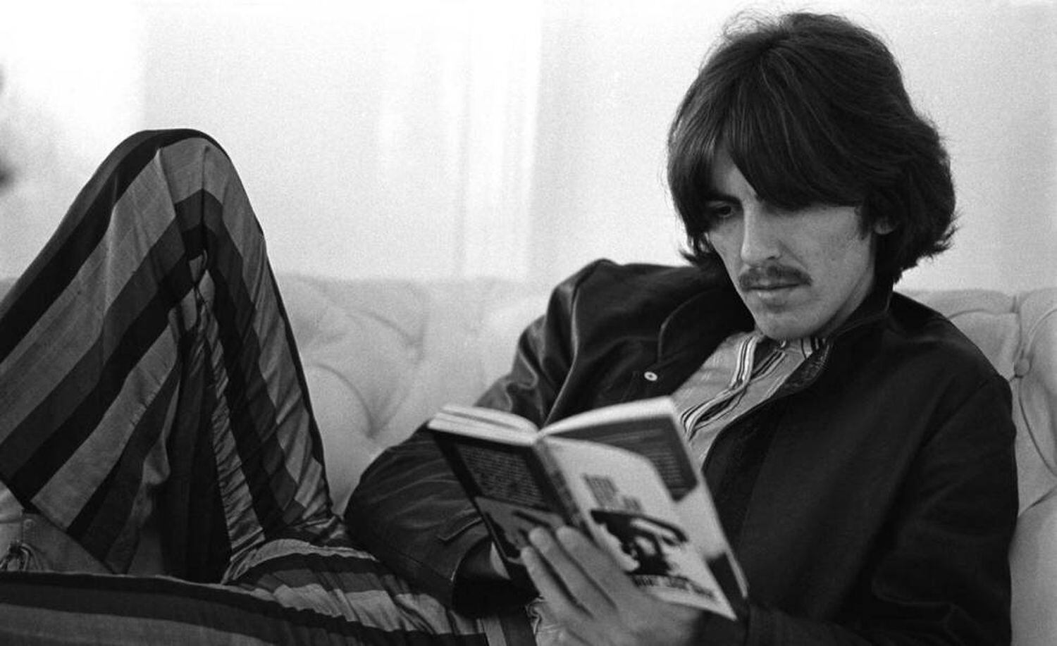 George Harrison lê livro de Bob Dylan em imagem de arquivo.
