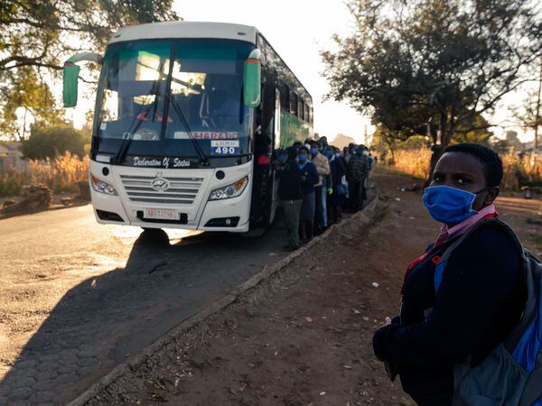 Passengers wearing face masks line up to board a government subsidised bus for transport to work in Harare on May 6, 2020. - The Zimbabwe government has made it mandatory for people to wear face masks in public during the COVID-19 coronavirus lockdown. (Photo by Jekesai NJIKIZANA / AFP)