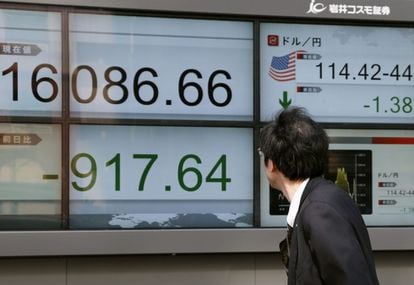 Empresários caminham junto a telas que mostram informação da Bolsa em Tóquio.