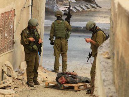 Soldados israelenses esperam ao lado de palestino morto a tiros.