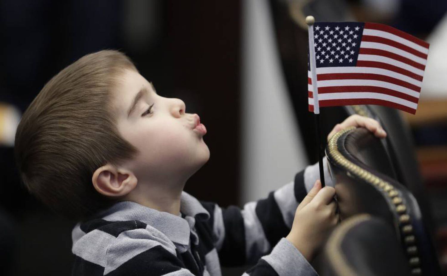Menino brinca com bandeira dos EUA durante cerimônia de naturalização da mãe.