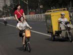 Condutor de um triciclo de carga observa duas moças que trafegam em uma bicicleta por uma rua de Pequim (China).