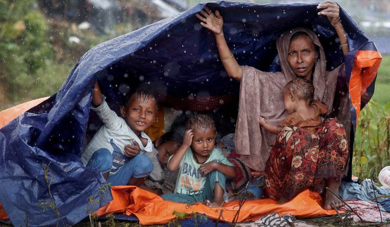 Refugiados da etnia rohingya se protegem da chuva com um plástico no campo de Cox’s Bazar, em Bangladesh