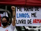 A demonstrator shouts slogans in front of a sign written in Portuguese that reads "I arm myself with books, I get rid of arms," during a protest against the government's response in combating COVID-19 and demanding the impeachment of Brazil's President Jair Bolsonaro, in Brasilia, Brazil, Saturday, Feb. 21, 2021. (AP Photo/Eraldo Peres)