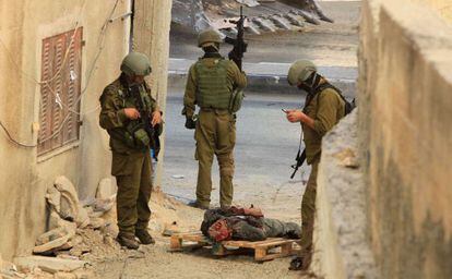 Soldados israelenses esperam ao lado de palestino morto a tiros.